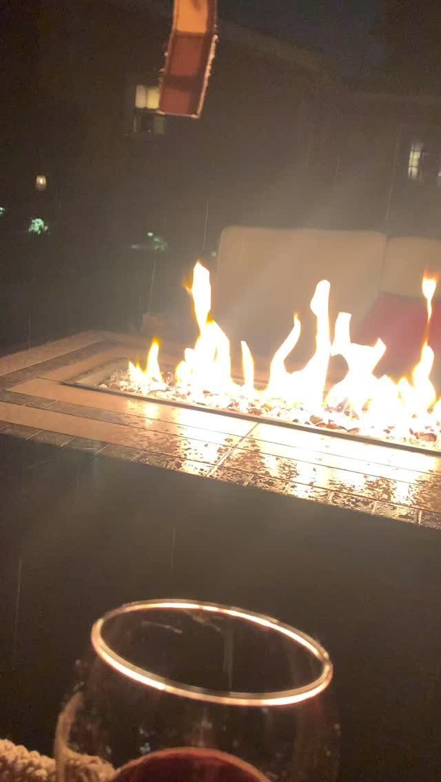 Flames burning brightly within a long, rectangular outdoor fire pit table at night.