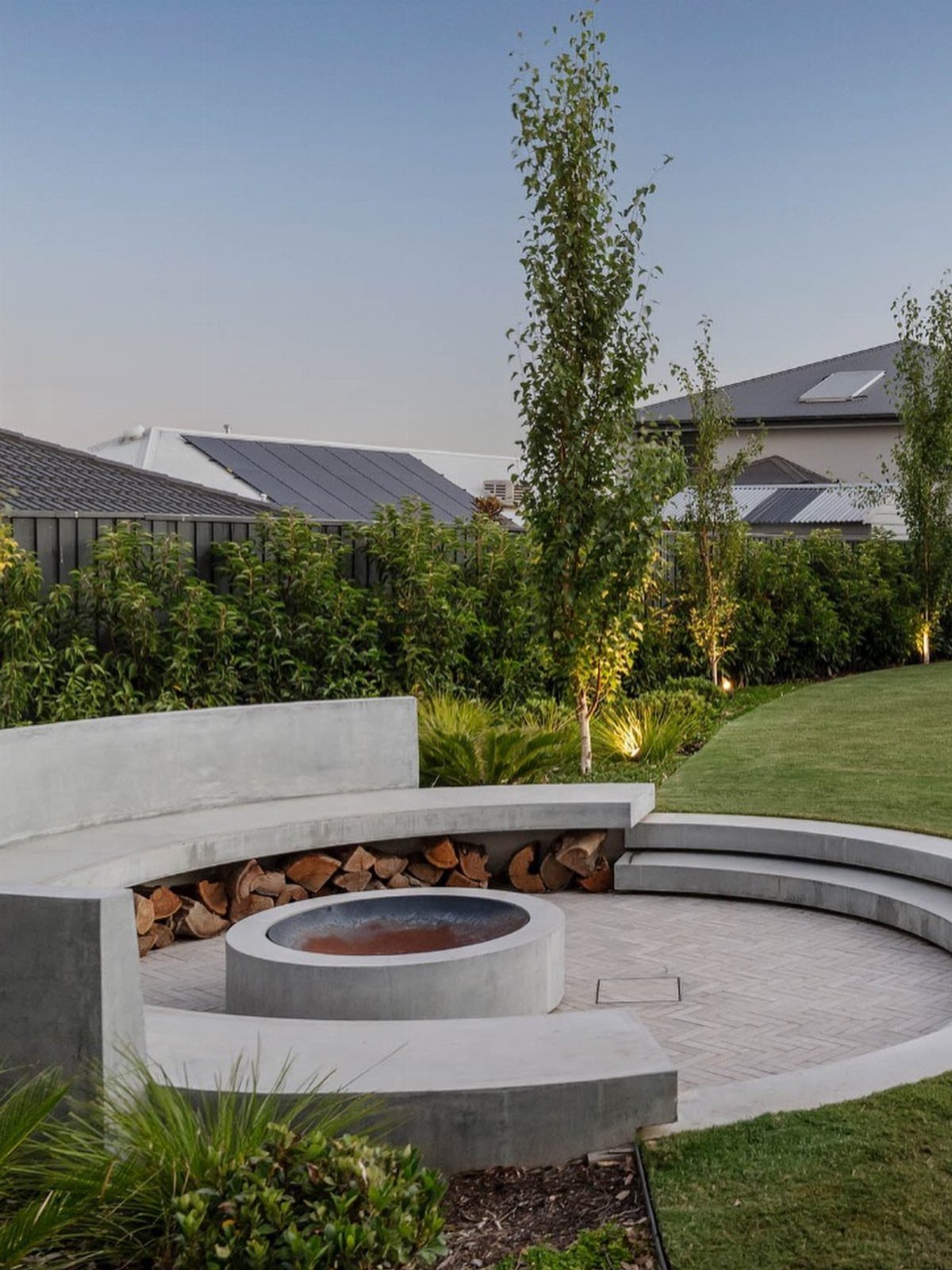 A modern concrete fire pit surrounded by a curved concrete seating wall in a backyard.