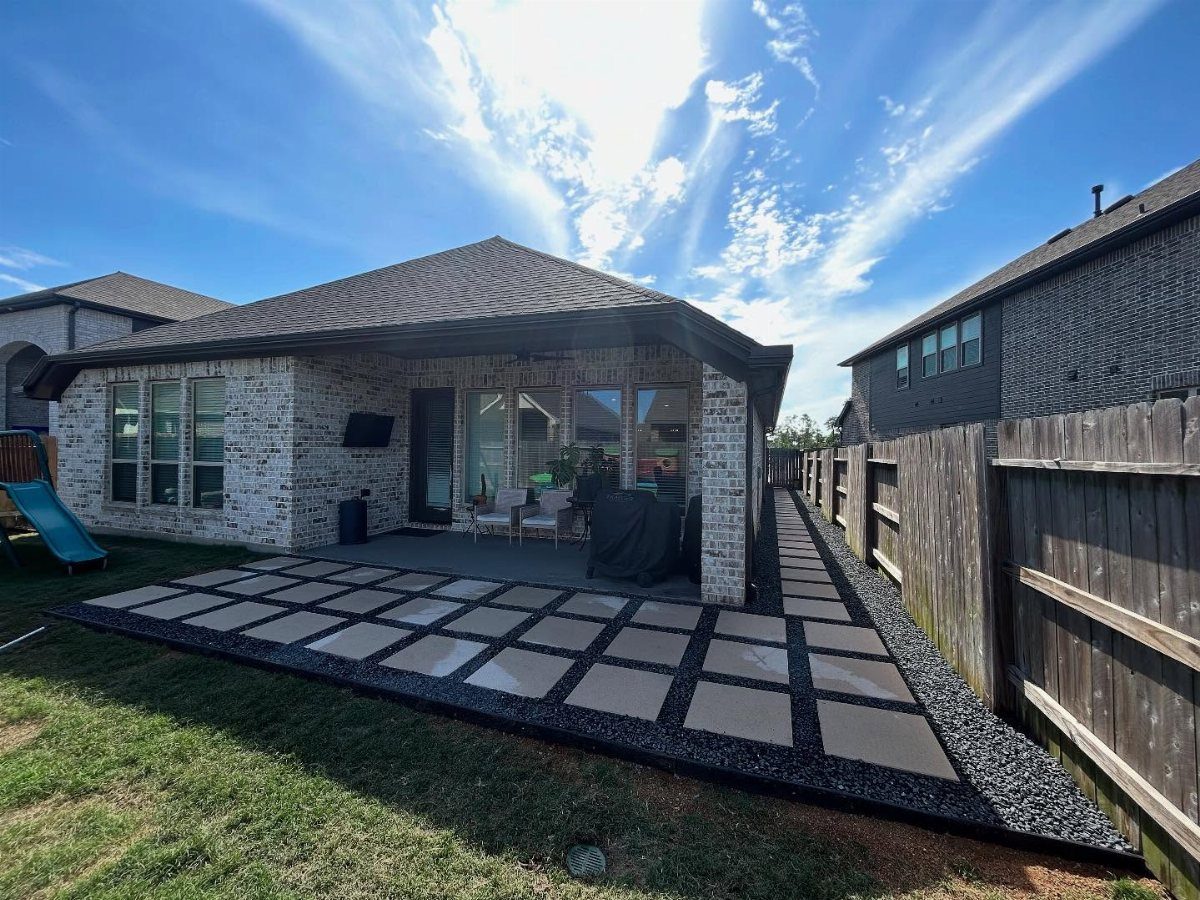 Large square concrete pavers with dark gravel in the joints form a patio next to a house.