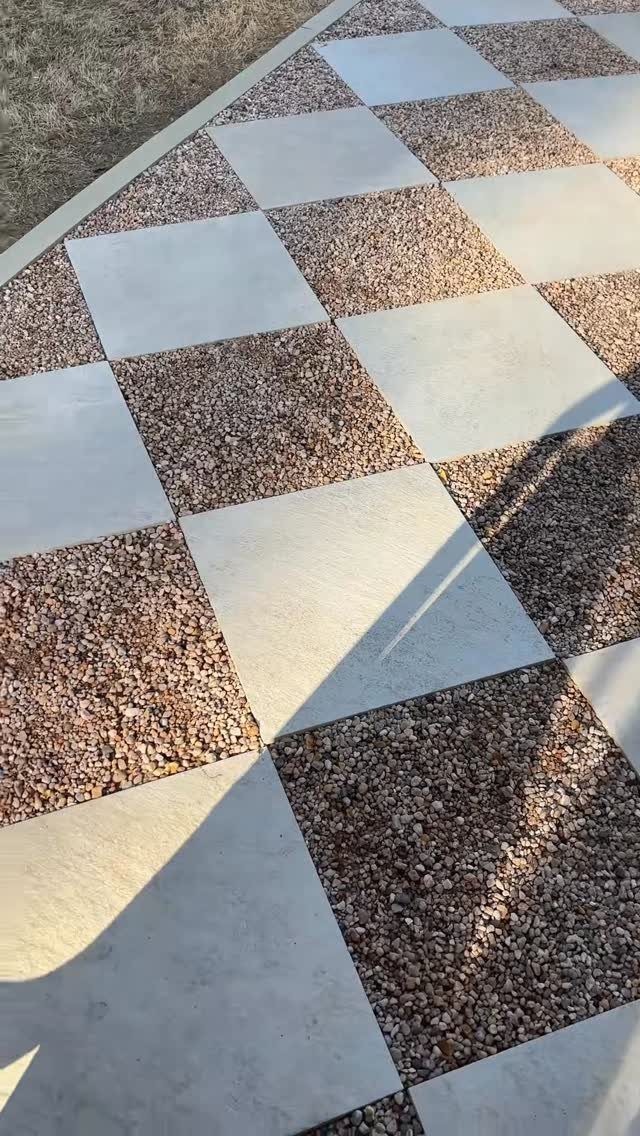 A checkerboard patio featuring alternating light grey concrete pavers and brown pea gravel squares.