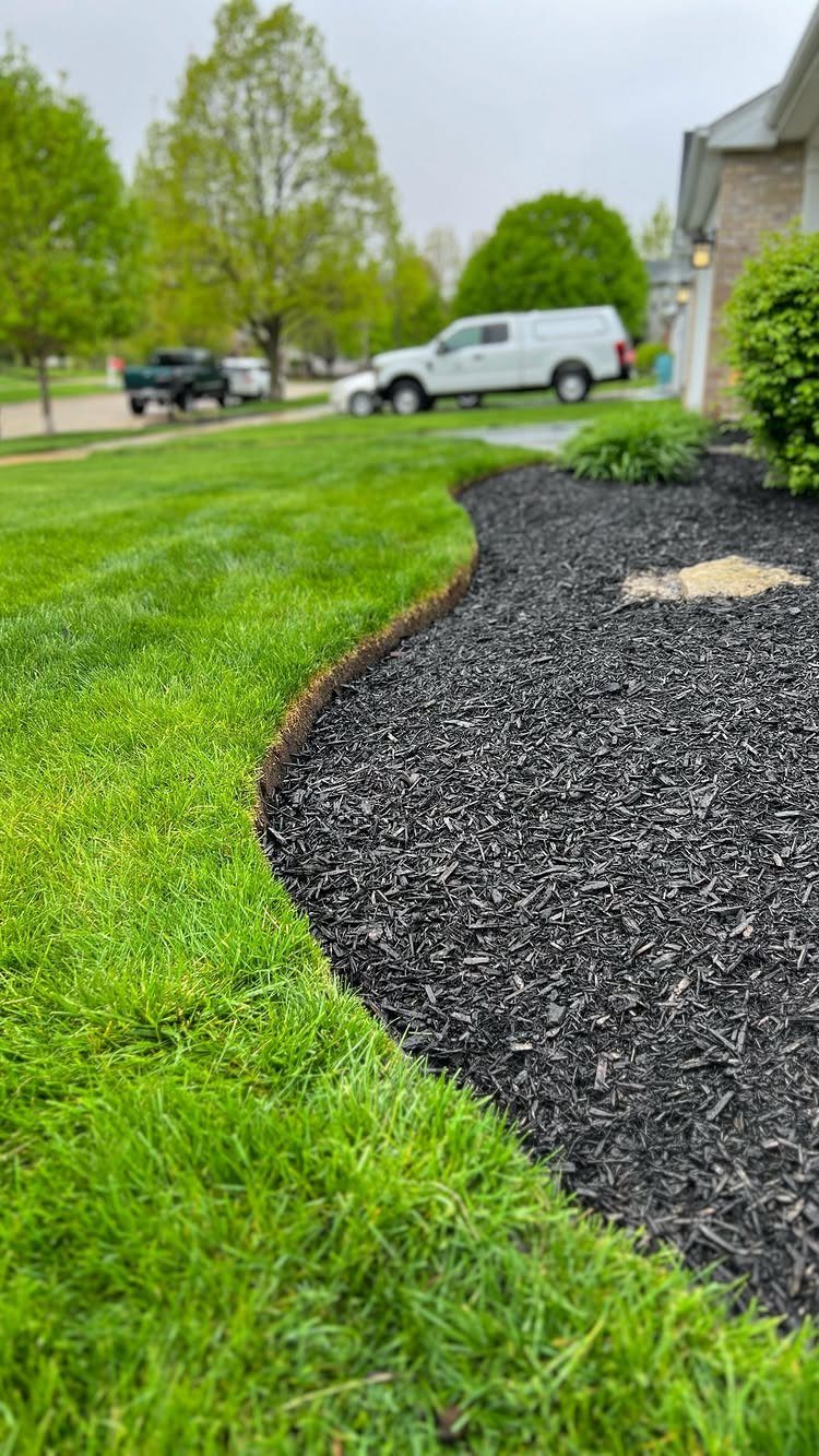 Dark black mulch in a curved garden bed next to a bright green lawn.