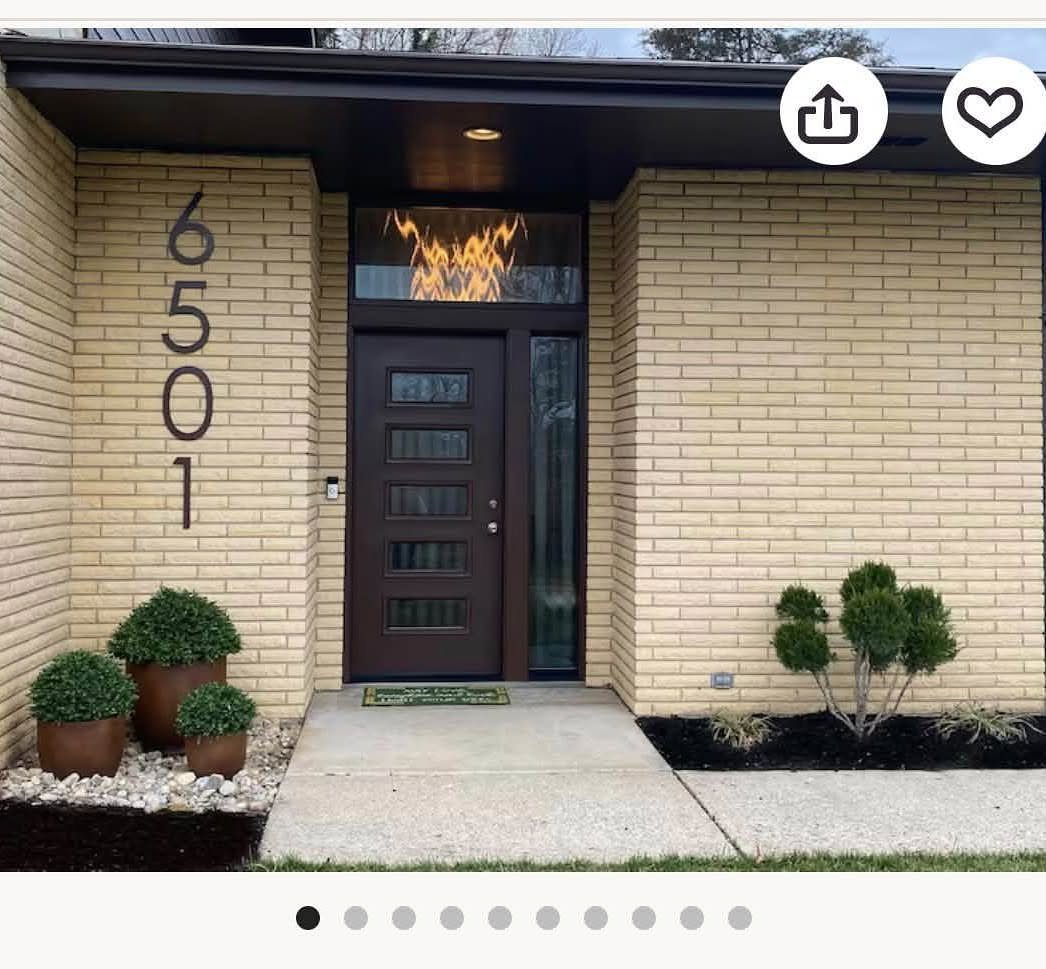 Large dark house numbers mounted vertically on a light tan brick exterior wall.