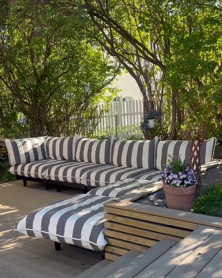 12 Deck Furniture Ideas: Layouts for Seating, Dining & Entertaining 9 Grey and white striped L-shaped sectional sofa on a wooden deck surrounded by green trees.