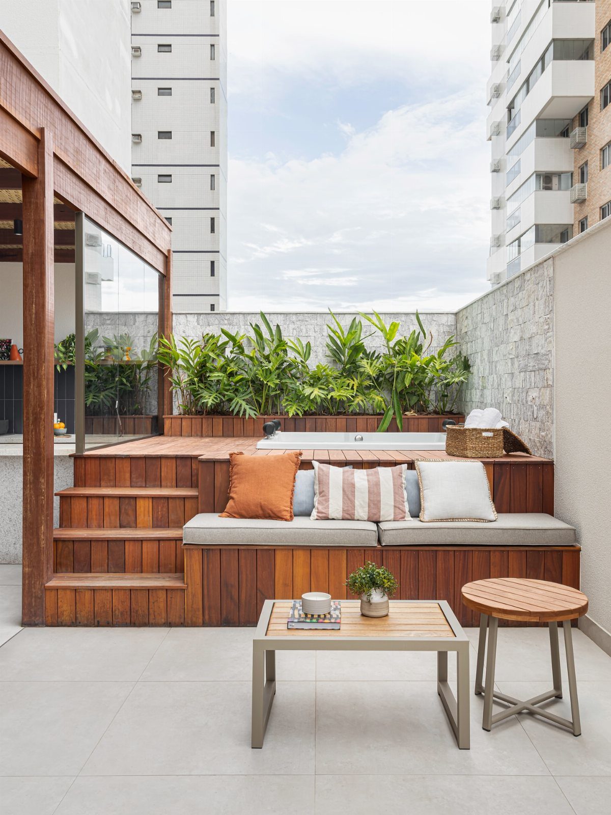 12 Deck Furniture Ideas: Layouts for Seating, Dining & Entertaining 4 Built-in wooden bench with cushions and pillows on a small urban terrace with plants.