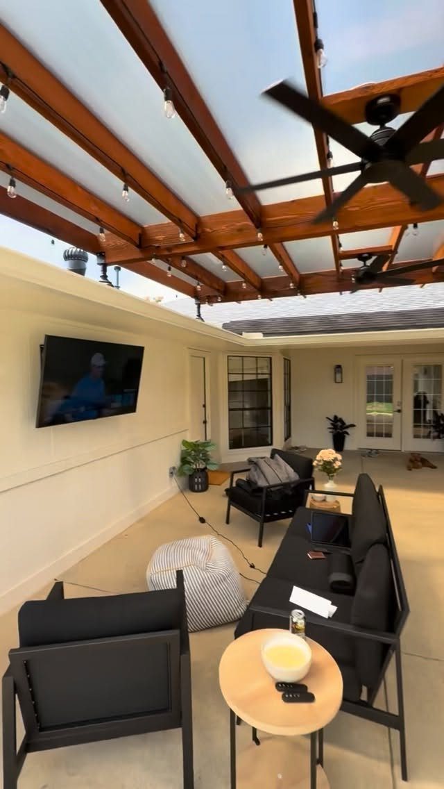 Wooden pergola with a translucent roof covering a modern outdoor patio with black furniture.