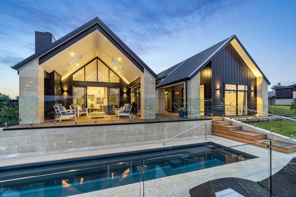 Modern house featuring two large dark metal gable roofs and a stone exterior wall.