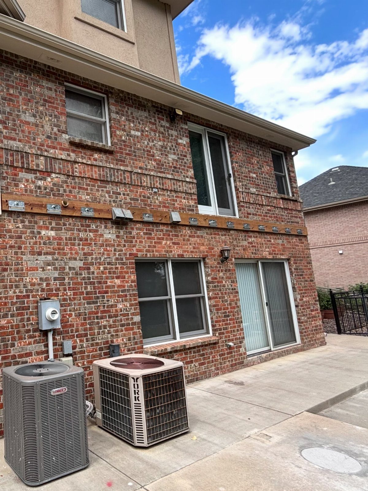 A wooden ledger board with metal brackets attached to a red brick house wall.
