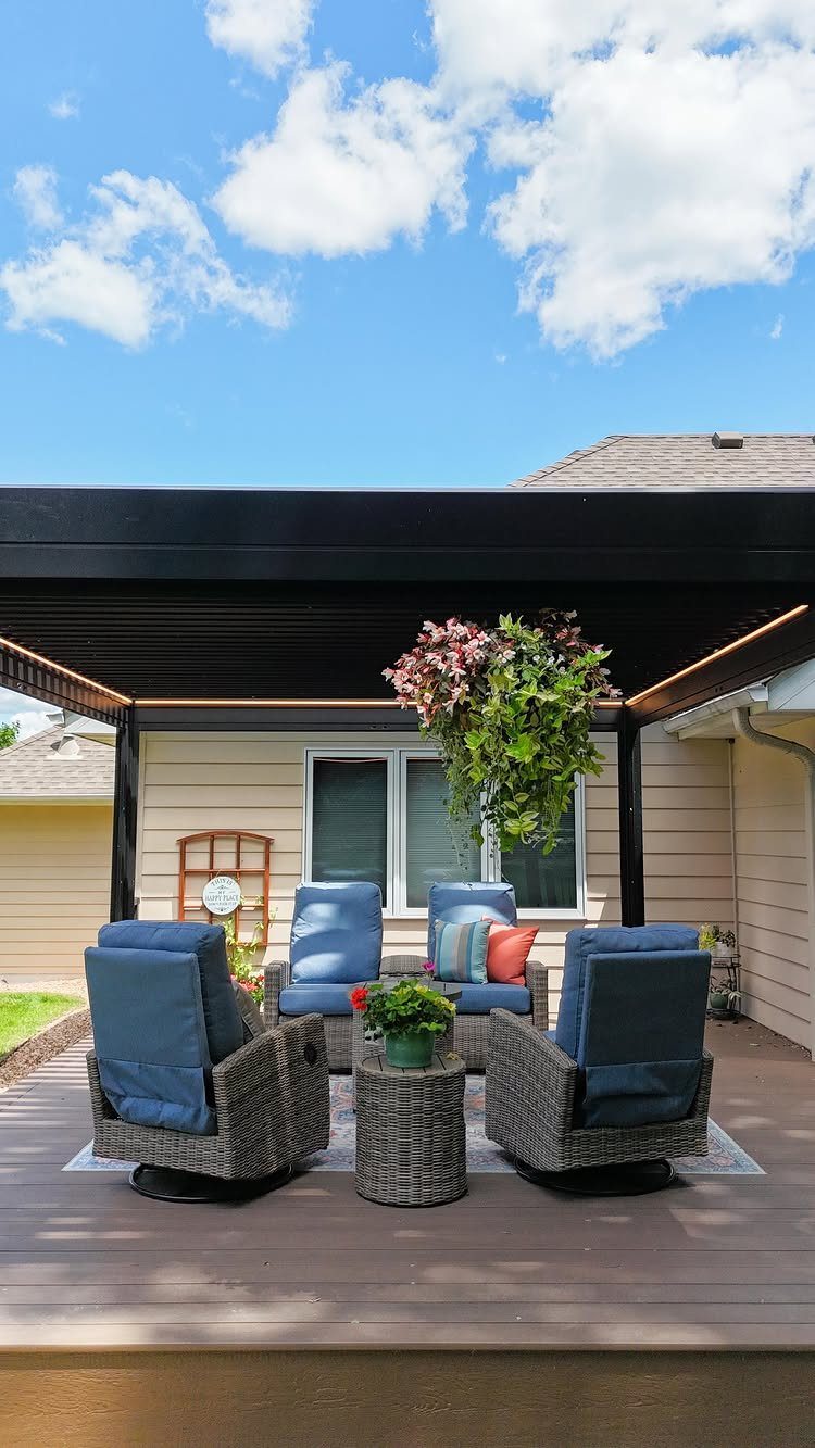 Modern dark flat roof covering a wooden deck with blue wicker patio furniture and plants.