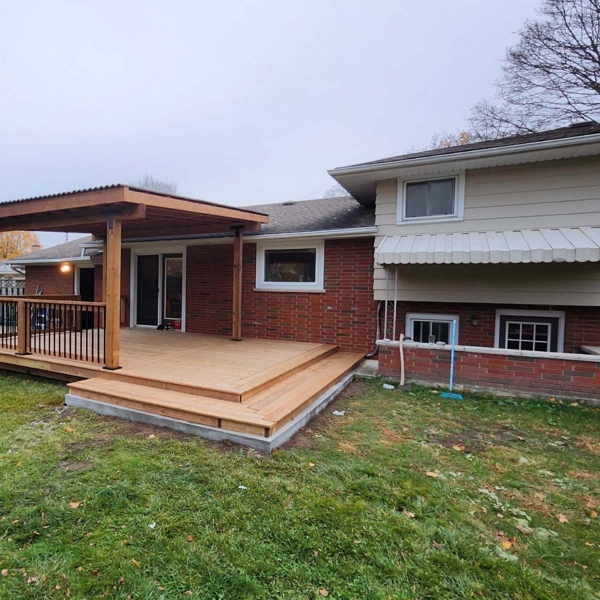Wooden deck with a corrugated metal roof supported by posts attached to a brick house.