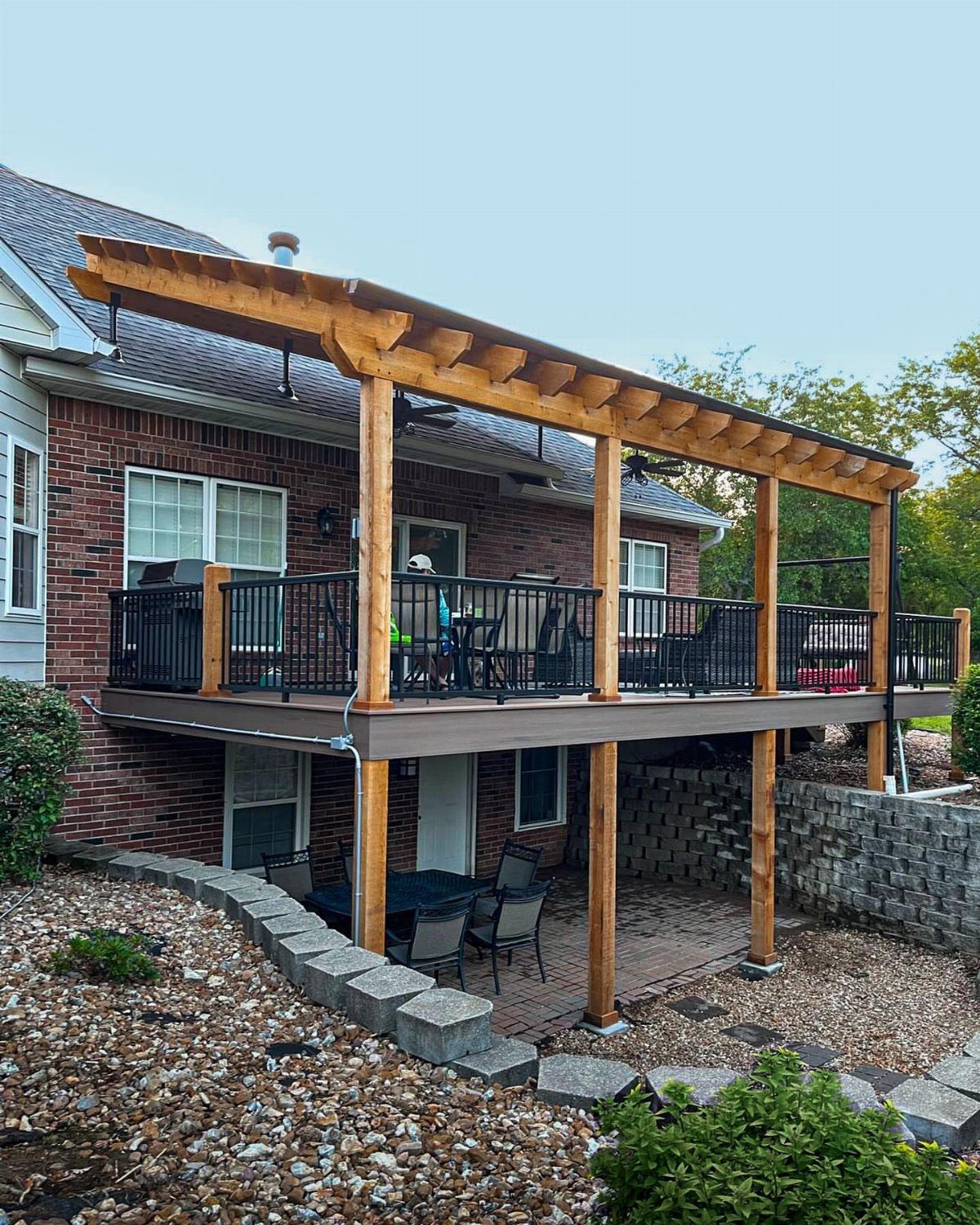 Wooden pergola roof with translucent covering attached to a brick house over a raised deck.