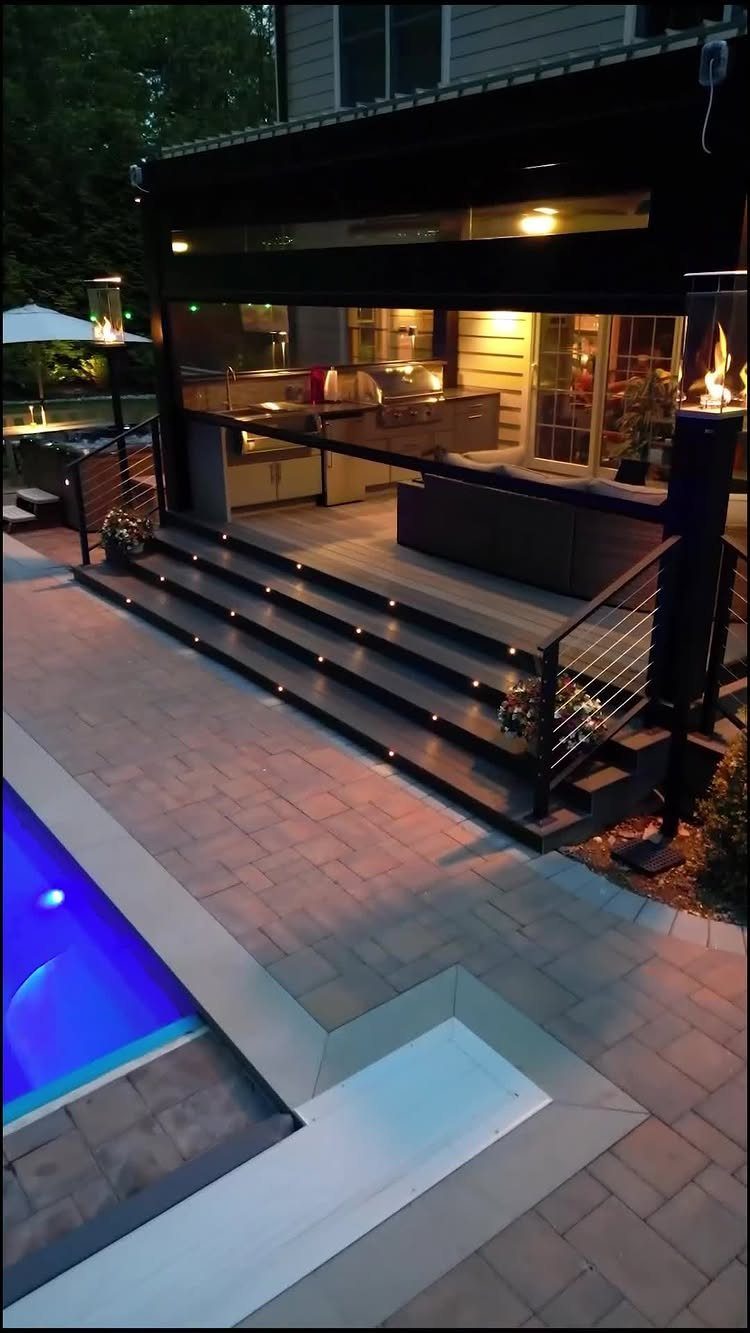15 Decks and Porches Back Patio Ideas for Outdoor Living 12 A modern dark wood deck with built-in lights, an outdoor kitchen, and a blue swimming pool.