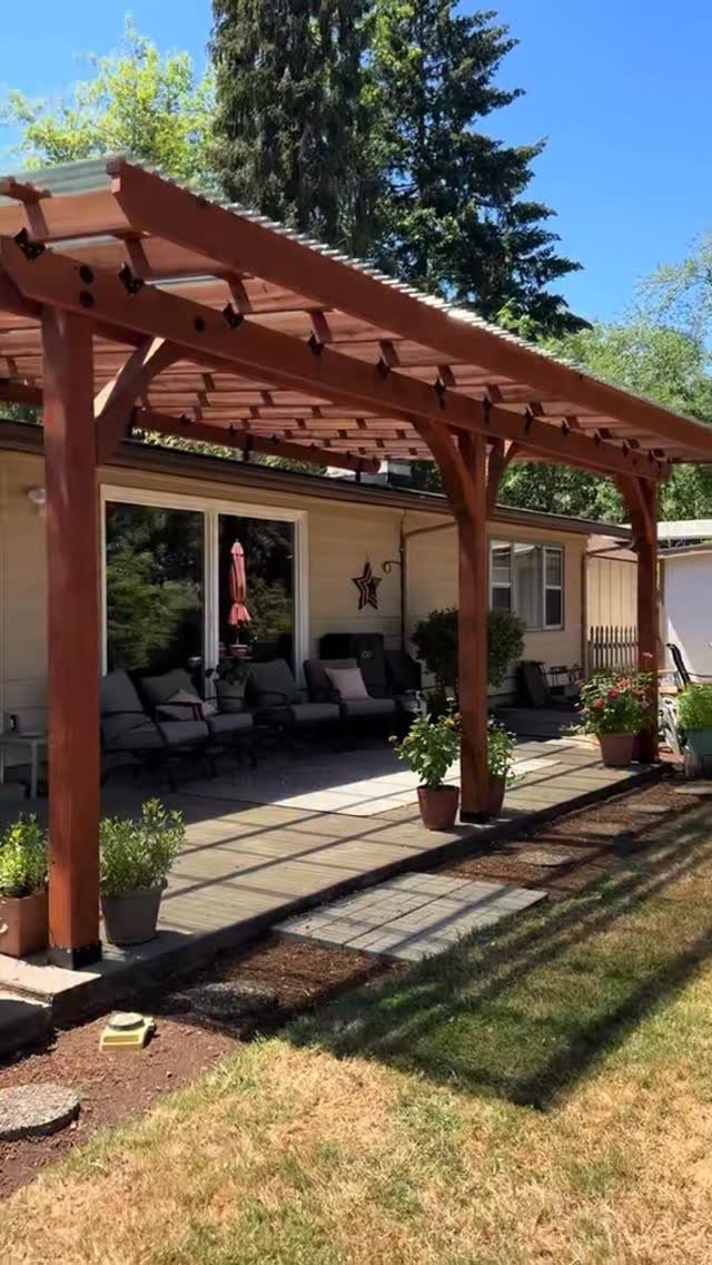 15 Decks and Porches Back Patio Ideas for Outdoor Living 4 A wooden pergola with a translucent roof covers a patio with lounge seating and potted plants.