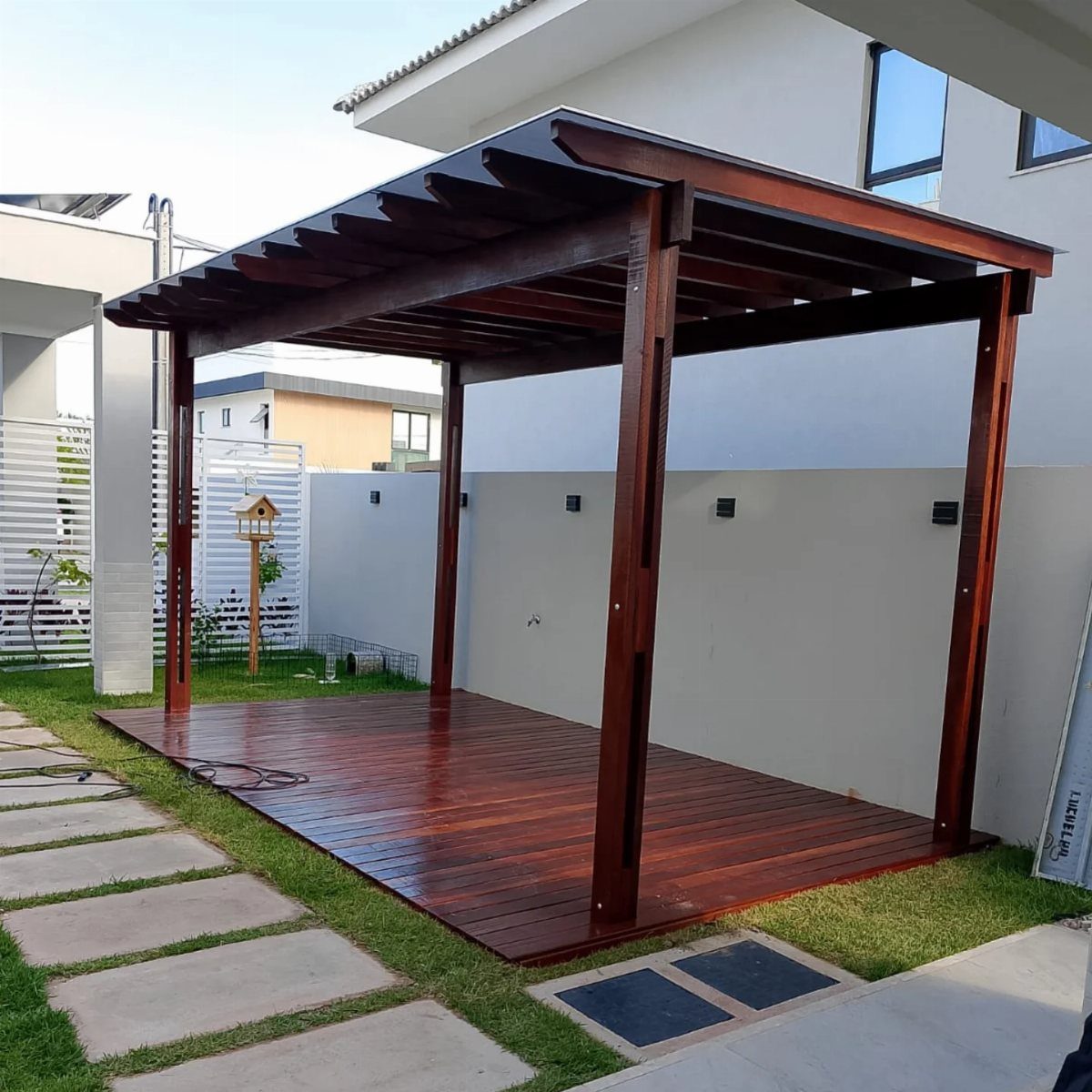 15 Decks and Porches Back Patio Ideas for Outdoor Living 9 A dark wood pergola covering a rectangular wooden deck situated on a green lawn next to white walls.