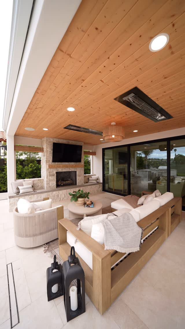 15 Decks and Porches Back Patio Ideas for Outdoor Living 13 A modern covered patio with a wood ceiling, stone fireplace, outdoor sofas, and large glass doors.