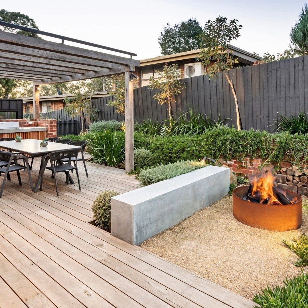 15 Decks and Porches Back Patio Ideas for Outdoor Living 7 Wooden deck with dining area, concrete bench, and a metal fire pit in a landscaped backyard.