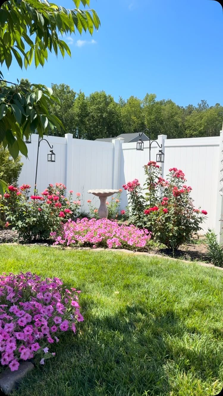 19 DIY Landscaping Ideas on a Budget for Any Yard 17 A stone birdbath centered among pink flowers and rose bushes in a sunny backyard garden.