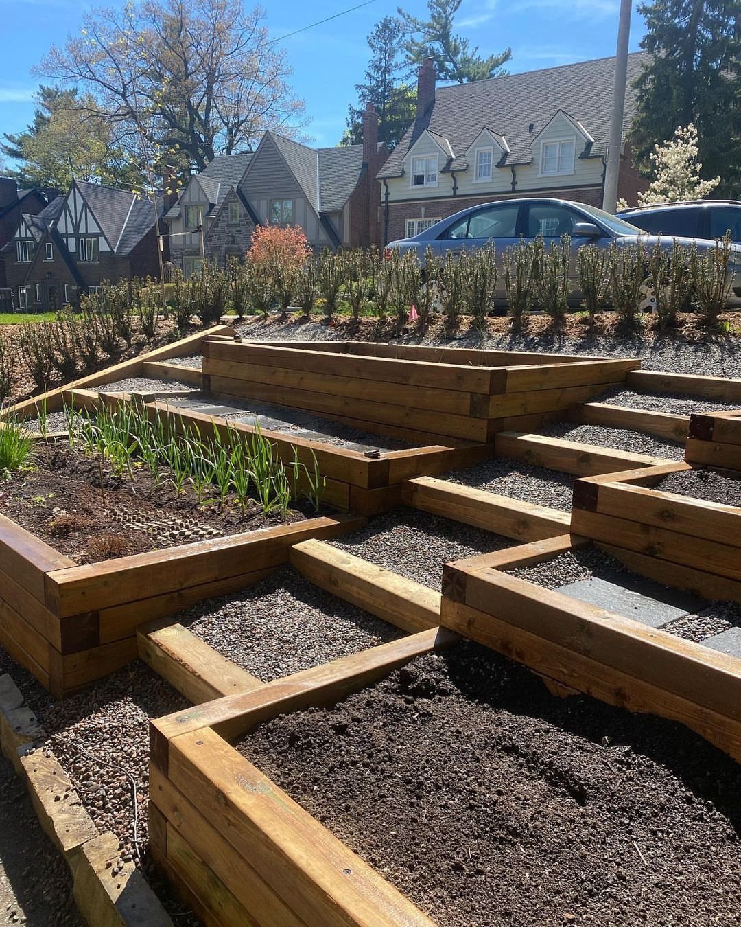 19 DIY Landscaping Ideas on a Budget for Any Yard 15 Wooden tiered planting beds filled with soil and gravel arranged on a sloped residential yard.