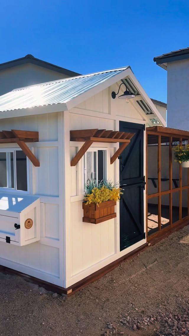 18 Farmhouse Backyard Ideas with Fire Pits, Herb Gardens & Outdoor Kitchens 15 A white wooden chicken coop with a metal roof and yellow flowers in a window planter.