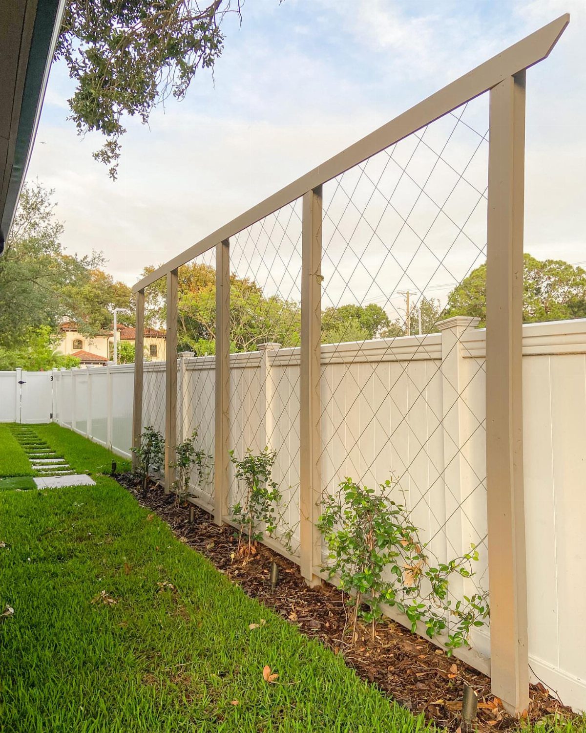 18 Farmhouse Backyard Ideas with Fire Pits, Herb Gardens & Outdoor Kitchens 5 A tall wooden trellis with wire mesh installed along a white fence in a backyard.