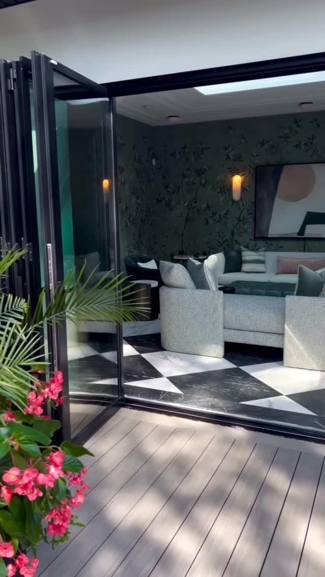 Modern sunroom with glass folding doors opening onto a wooden deck with pink flowers.