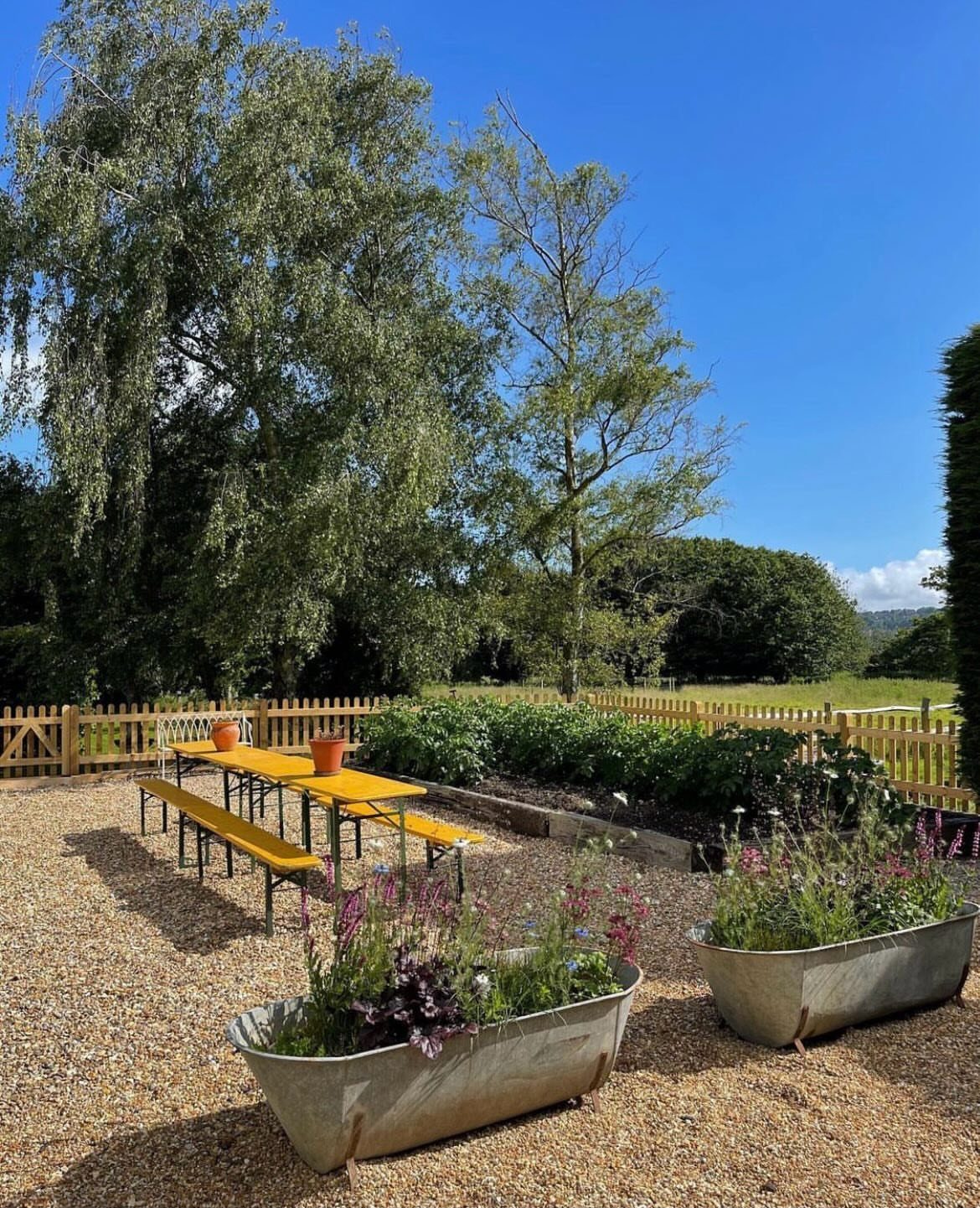 Two galvanized metal troughs filled with colorful flowers sit on a gravel garden area.
