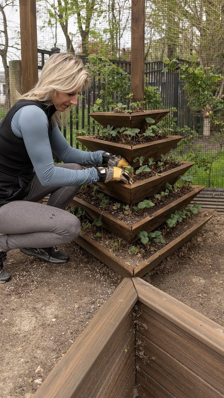 A woman tending to plants in a tiered wooden pyramid planter in a garden.