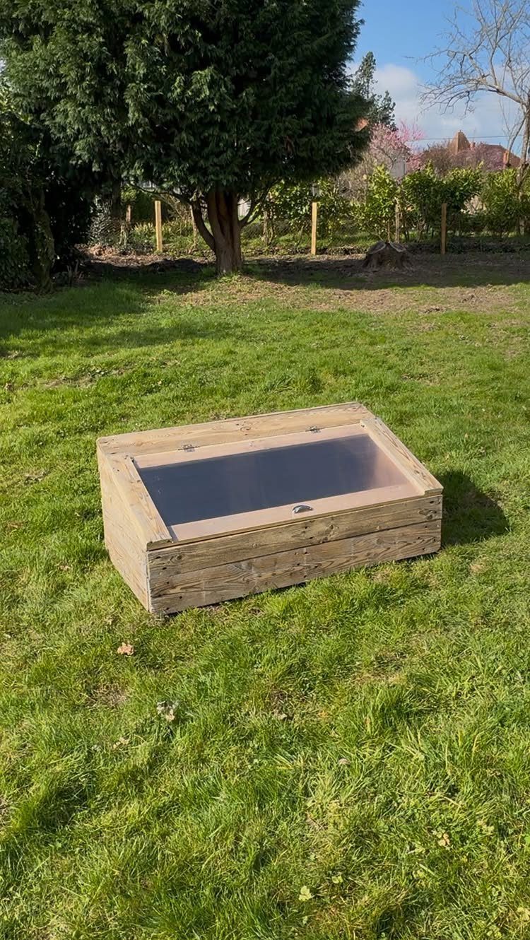 Greenhouse Using Pallets: 5 Builds for Small Yards 2 A wooden cold frame with a clear top sits on a green grass lawn.