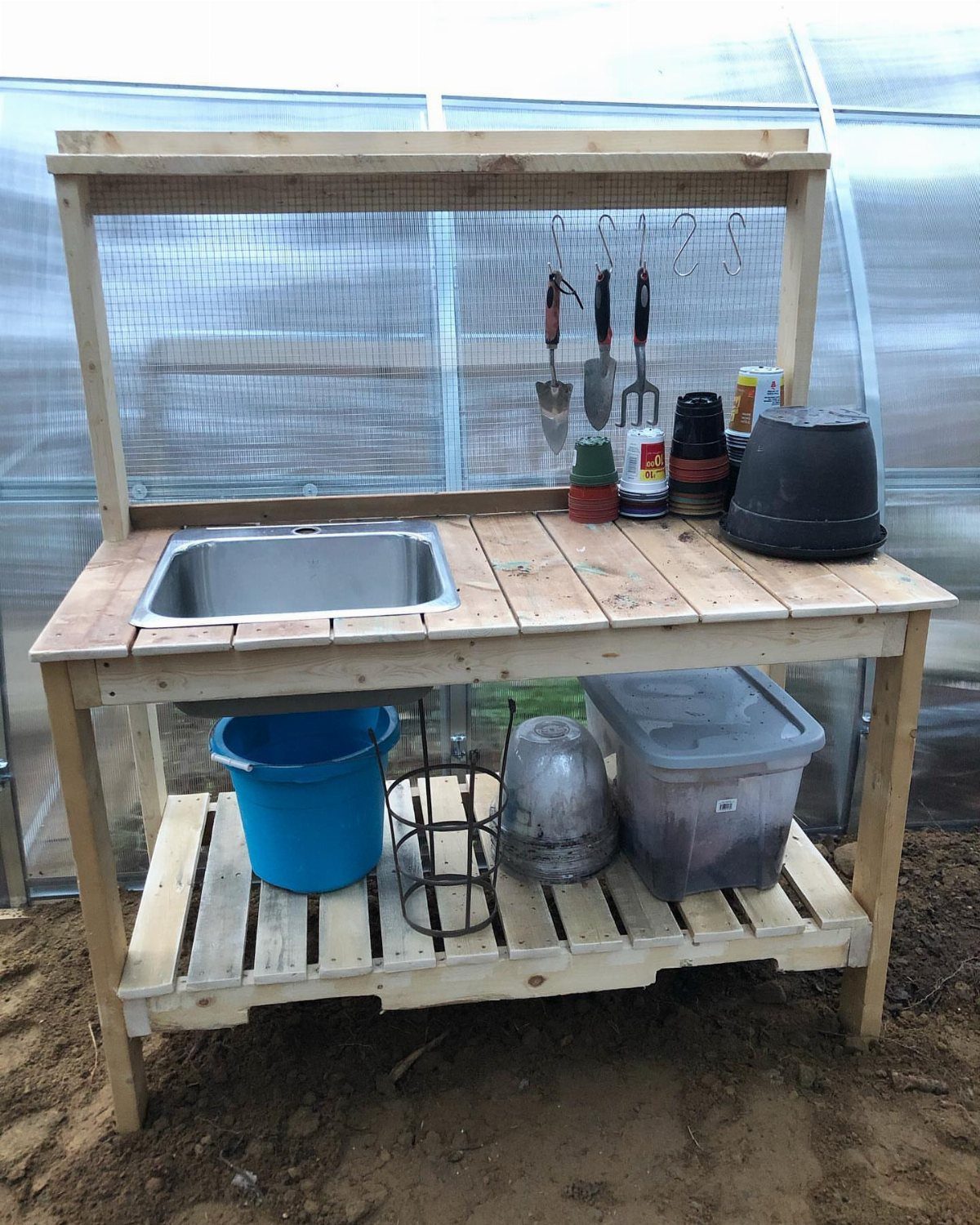 Greenhouse Using Pallets: 5 Builds for Small Yards 1 Wooden workbench with a built-in sink and gardening tools in a greenhouse setting.