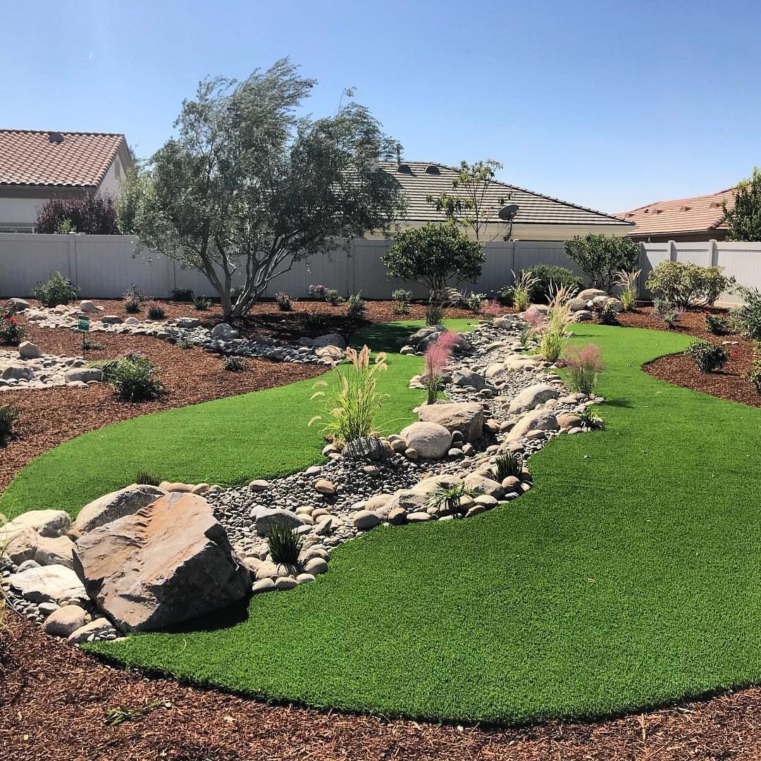 A winding dry creek bed of rocks and pebbles flowing through a lush green lawn.
