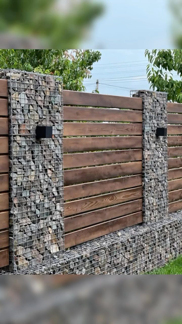 A modern fence composed of dark wood slats and stone-filled wire gabion cages.