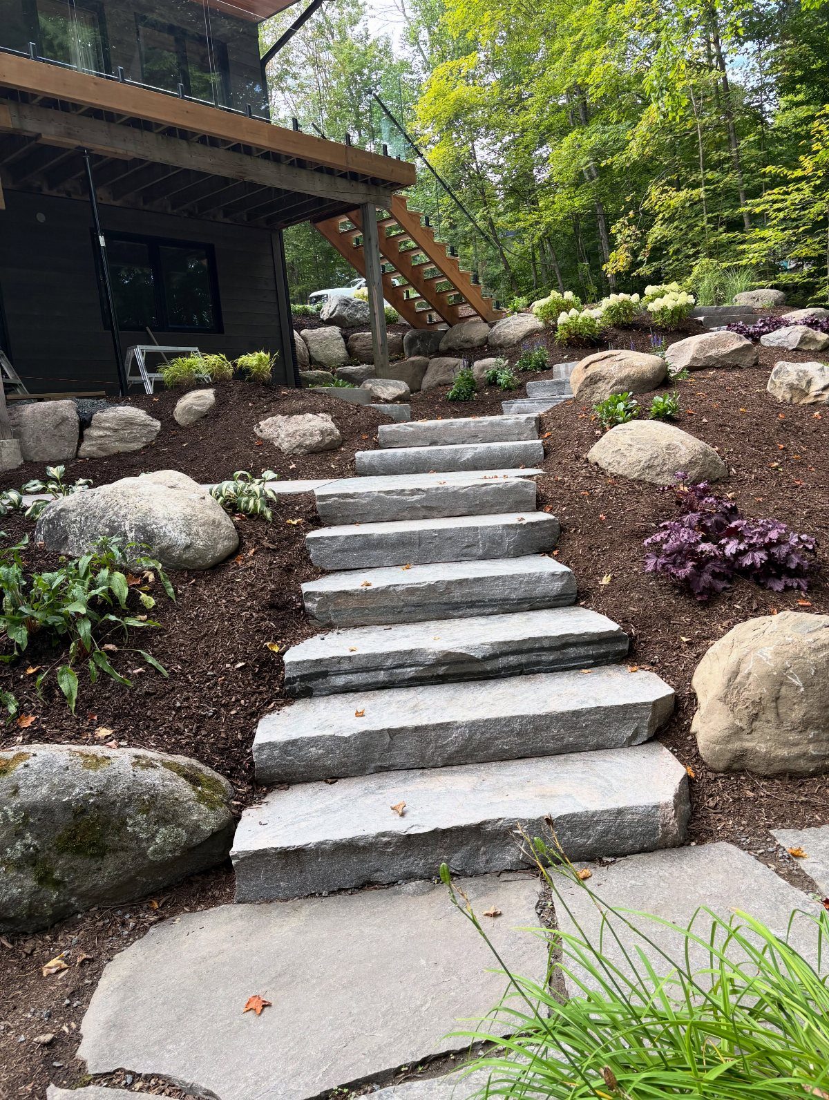 Flat grey stone slabs form a natural staircase through a landscaped garden bed with boulders.