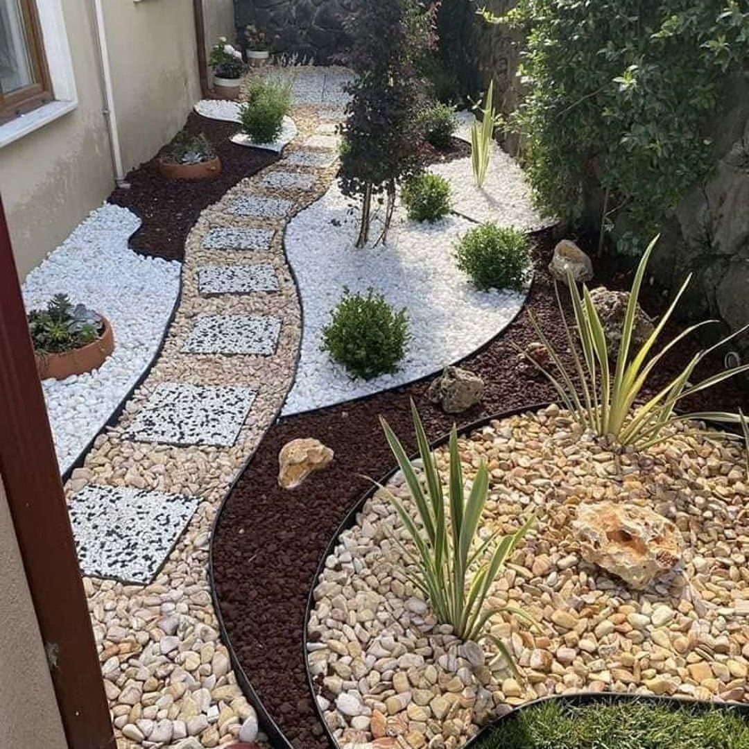 A winding stone pathway surrounded by white pebbles, dark mulch, and tan gravel in a garden.