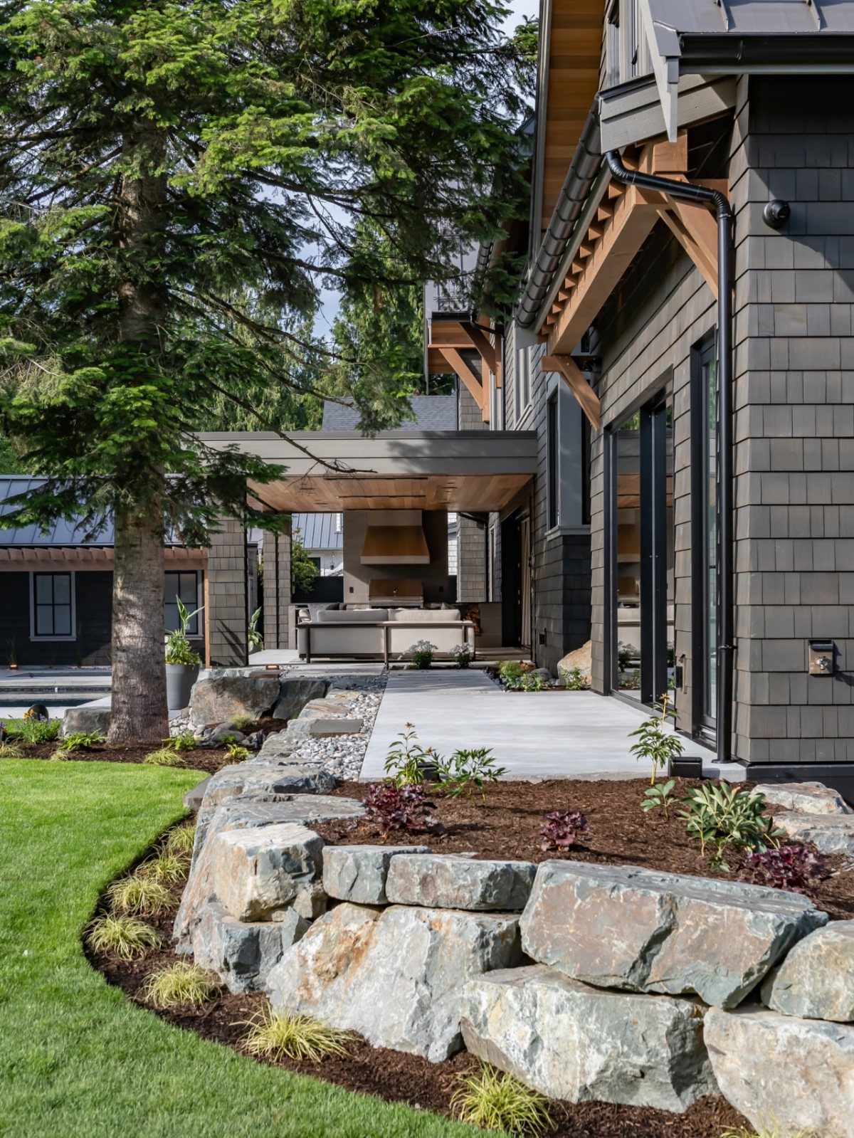 Large grey boulders forming a low retaining wall next to a dark mulch garden bed and green lawn.