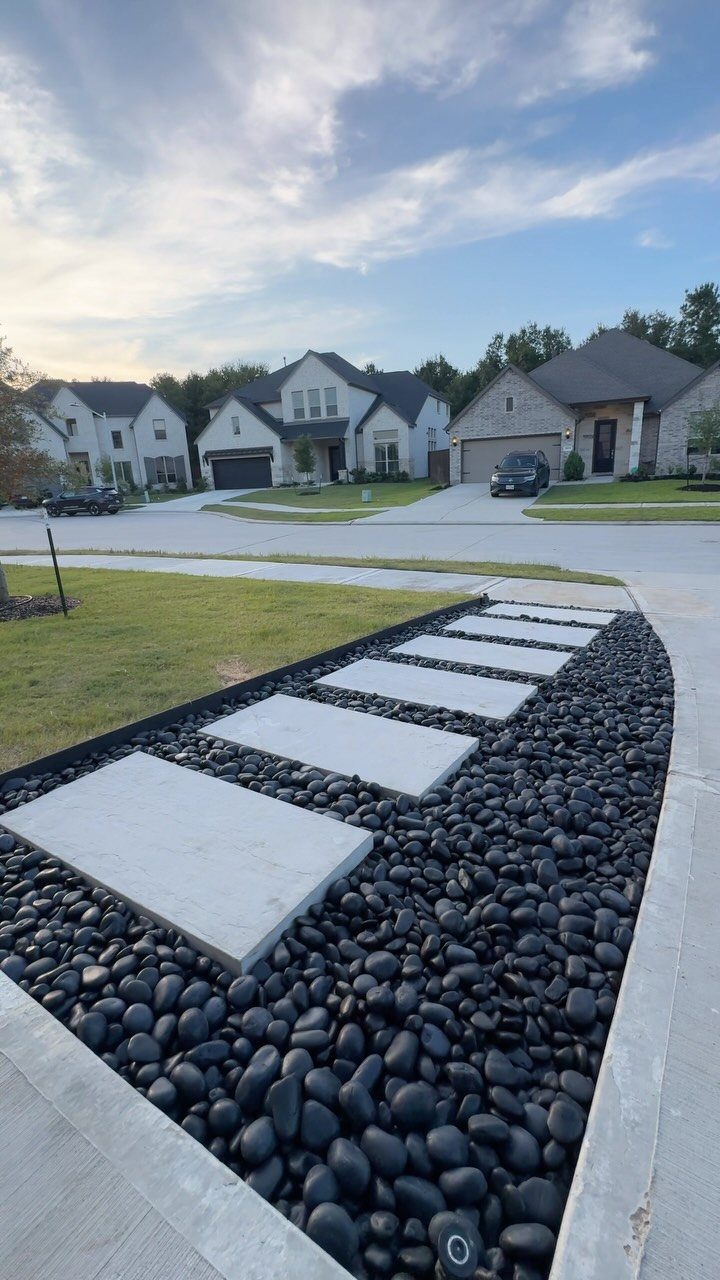 Black river stones and rectangular concrete pavers lining a sidewalk in a residential yard.