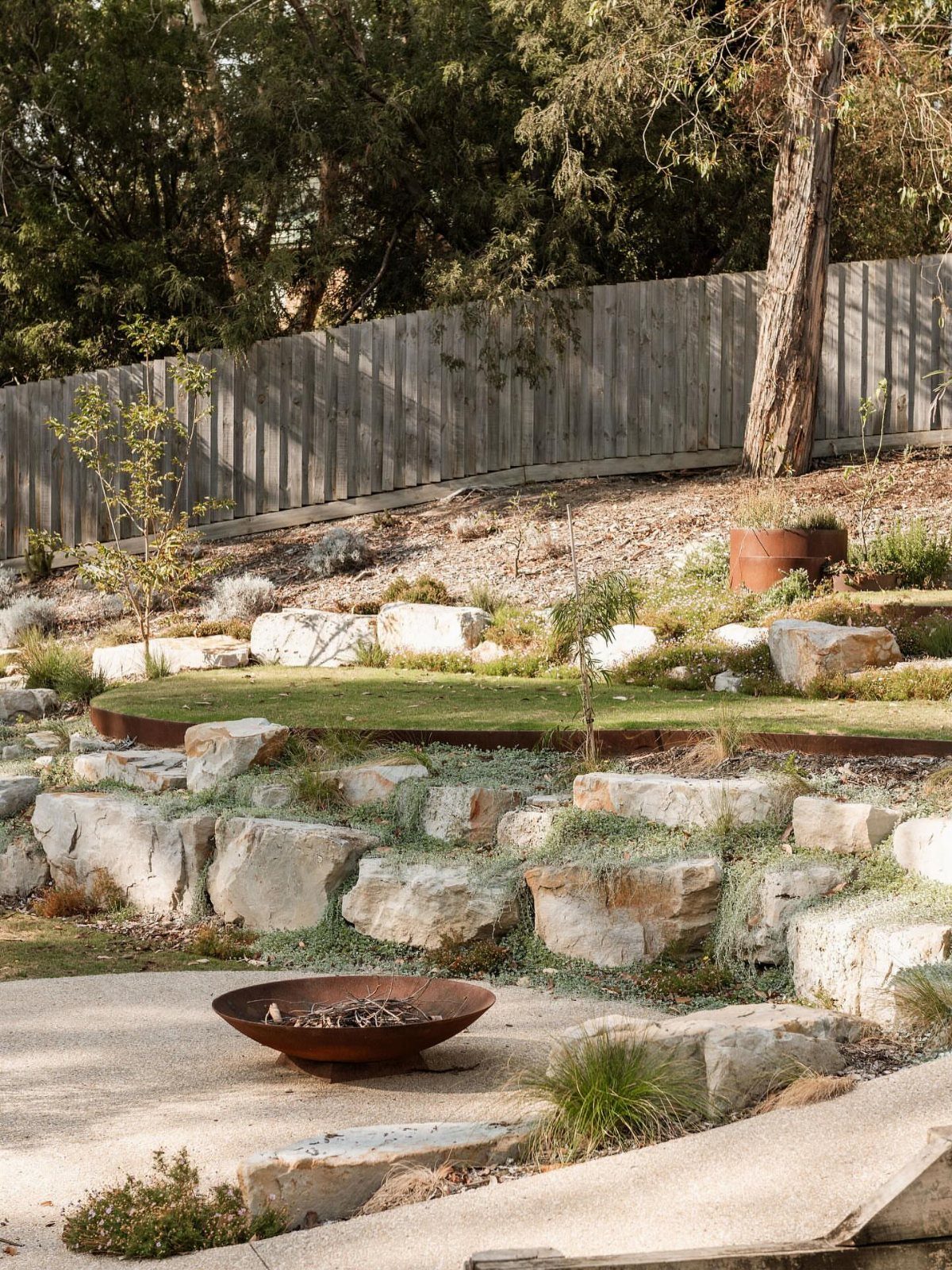 Large stone blocks create terraced levels in a landscaped garden with grass and plants.