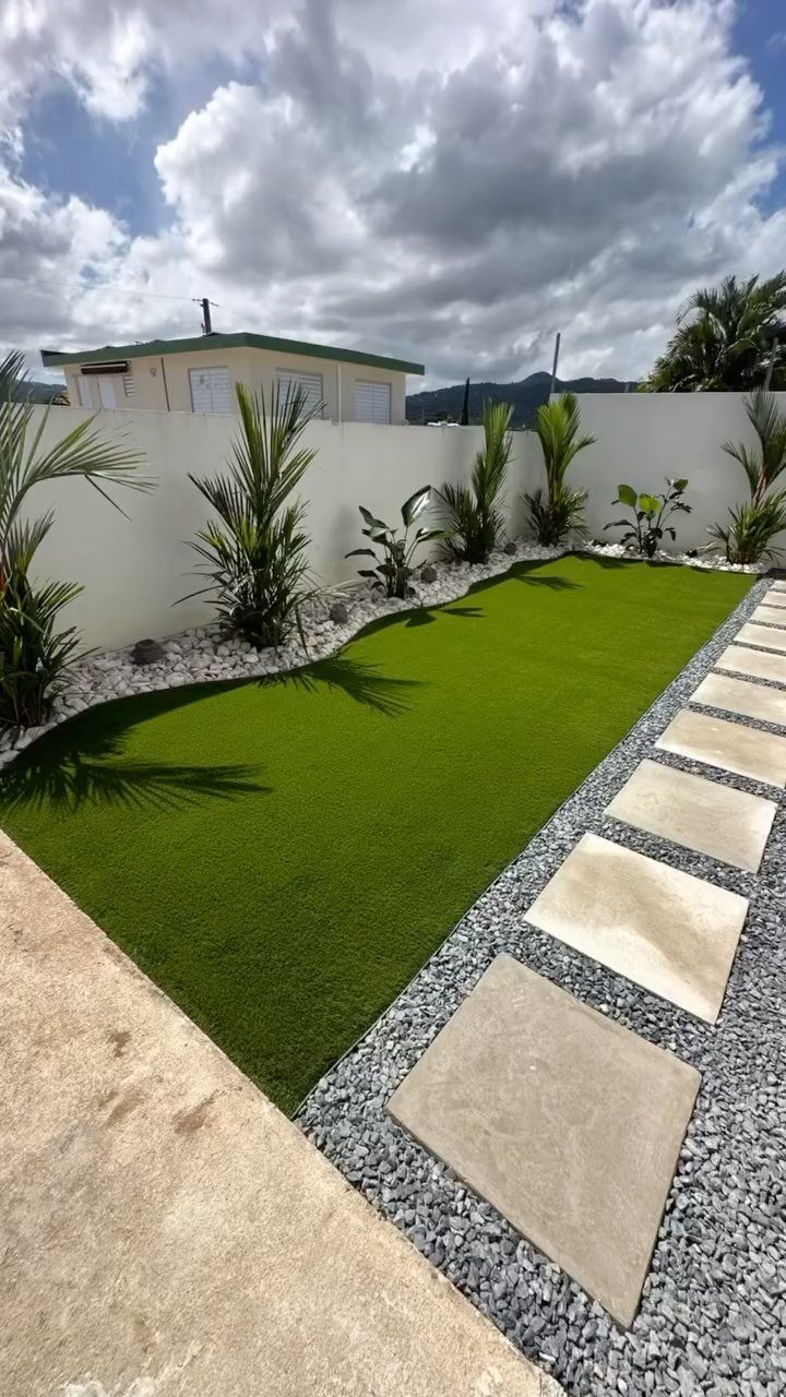 Artificial turf patch with stepping stones and tropical plants in a small patio garden.