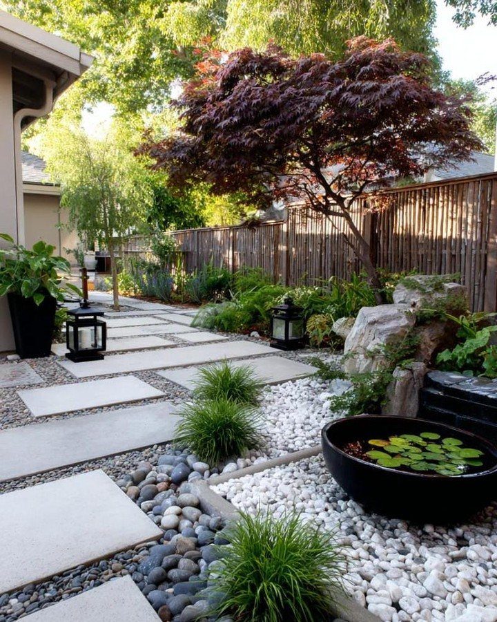 Concrete pavers and white pebbles create a modern path through a landscaped garden with plants and trees.