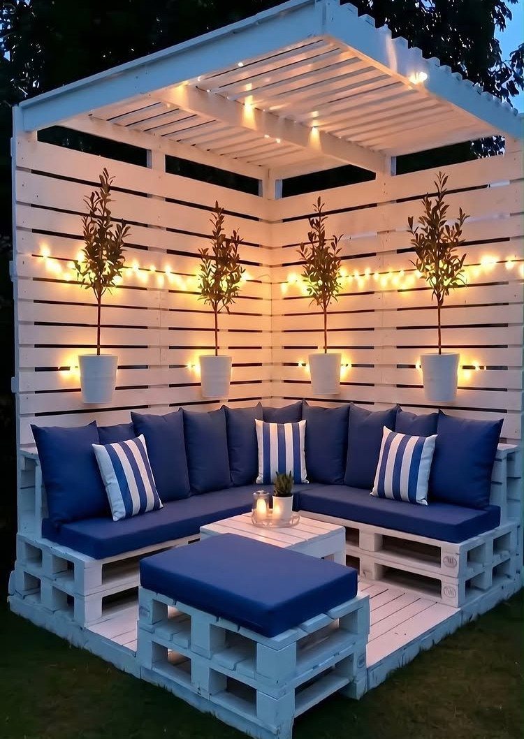 White pallet lounge furniture with blue cushions and string lights under a pergola.