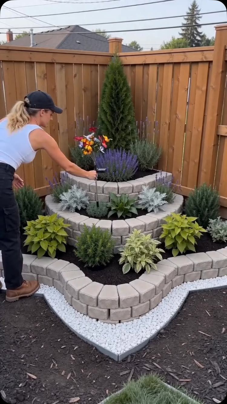 A woman gardening in a multi-tiered stone planter bed filled with diverse green and purple plants.
