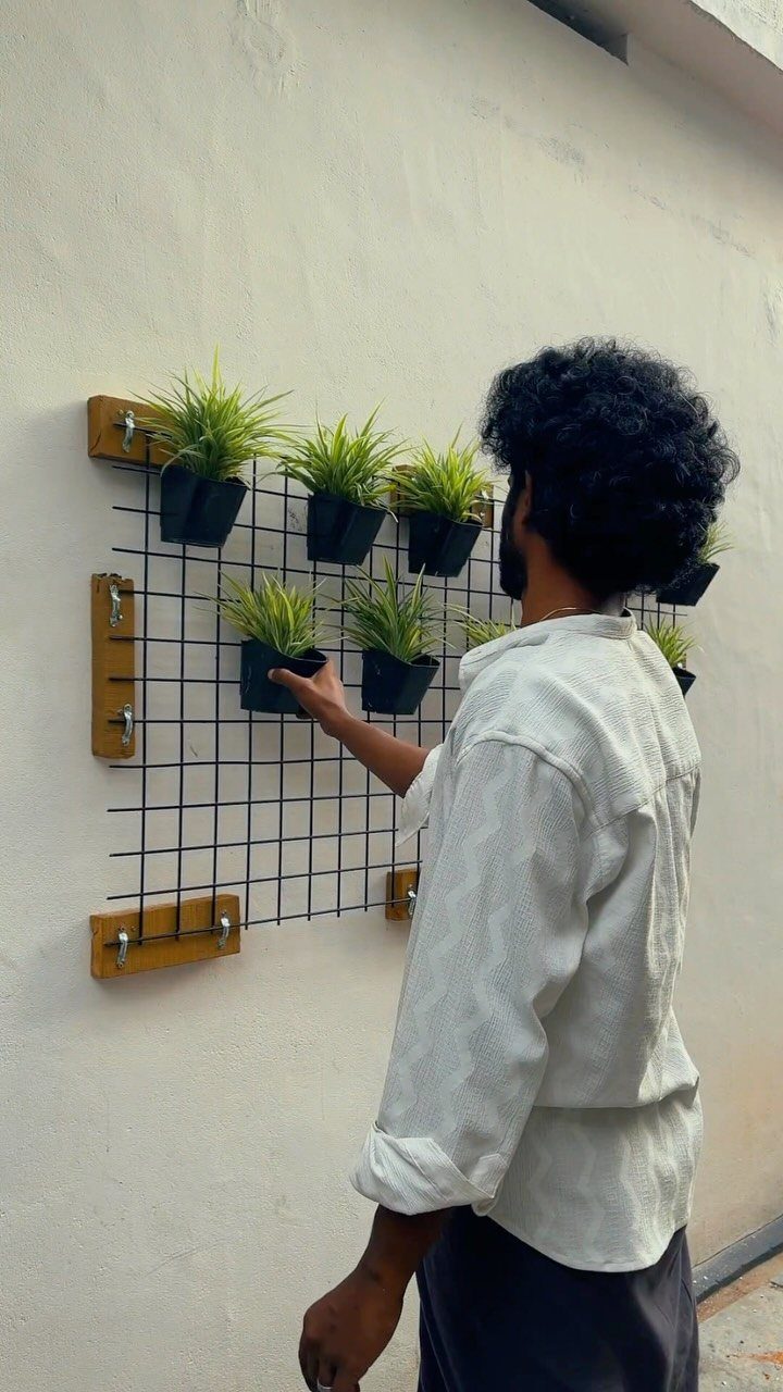 A man adjusts small green plants in black wall-mounted planters attached to a wire grid.