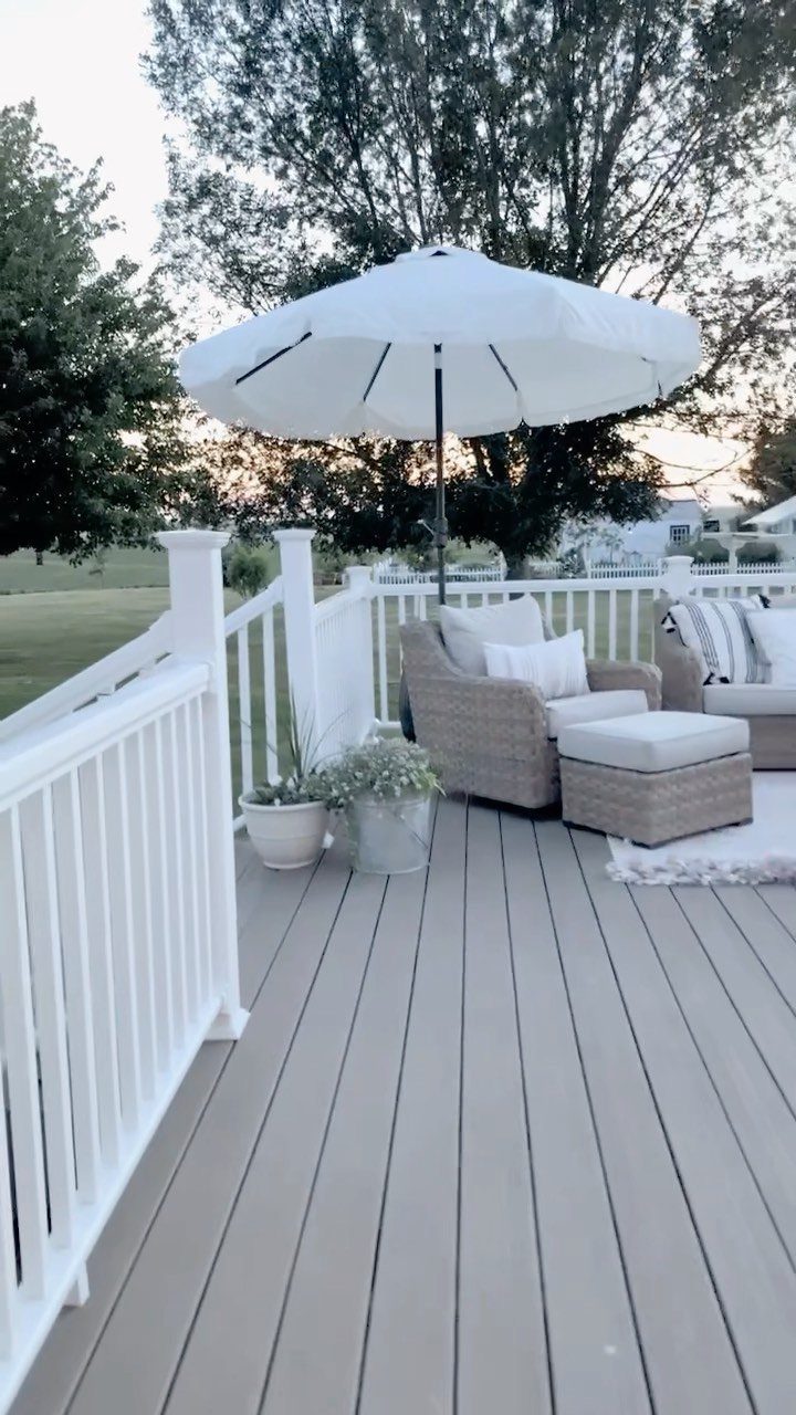 Wicker lounge furniture with white cushions and a large white umbrella on a grey deck.