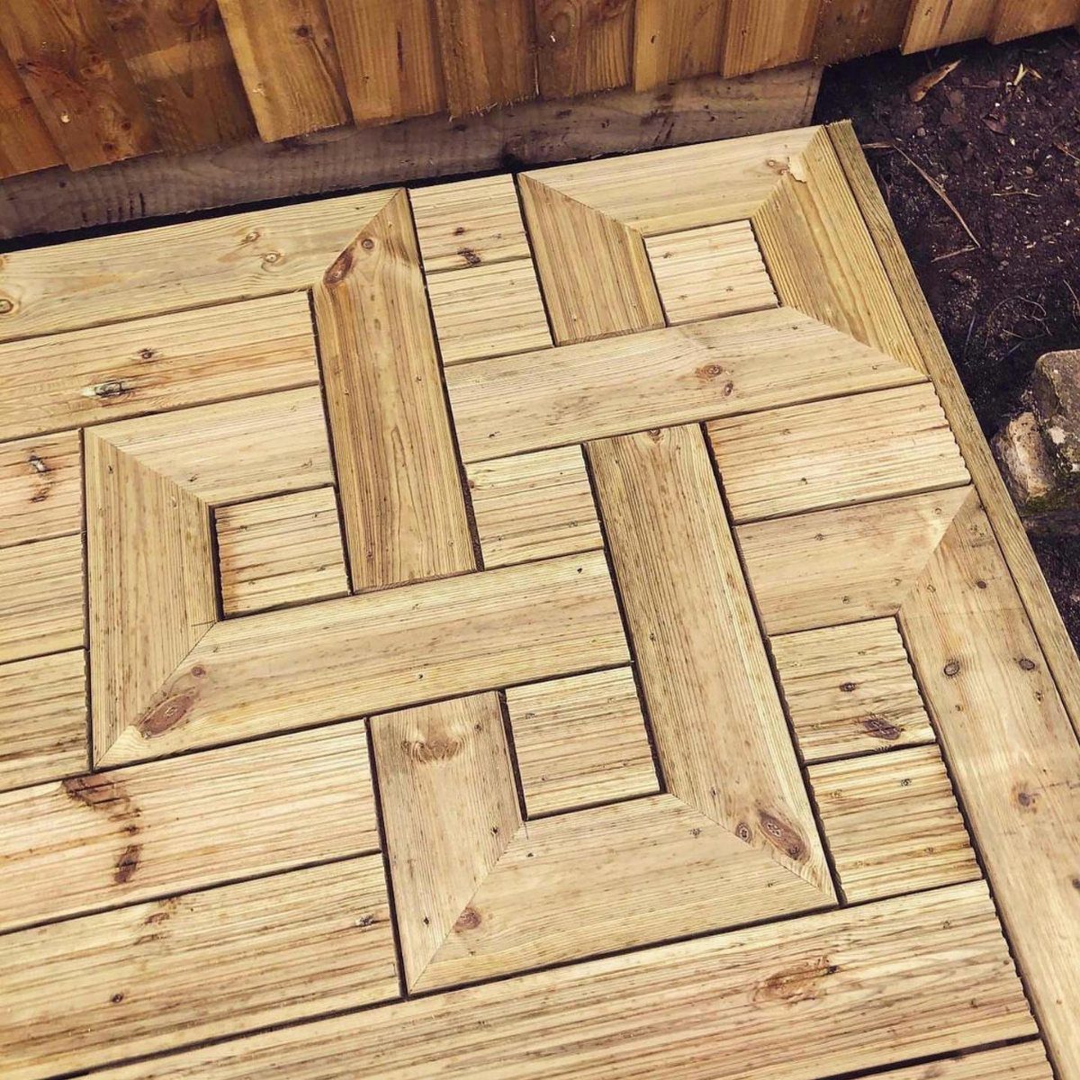 Wooden deck boards arranged in an intricate geometric parquet pattern with interlocking square designs.