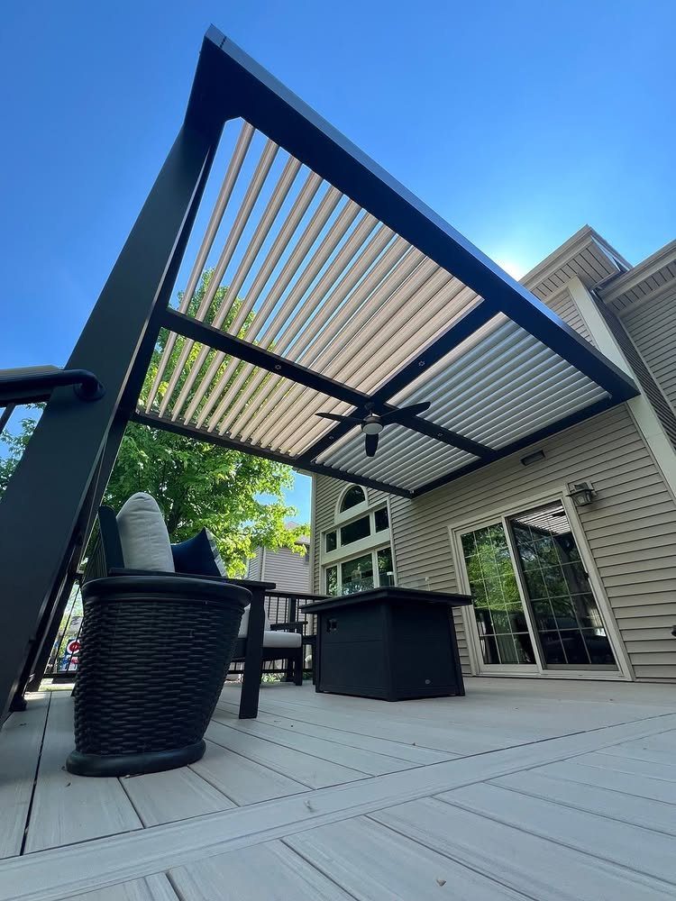 A dark metal louvered pergola with a ceiling fan over a grey composite deck.