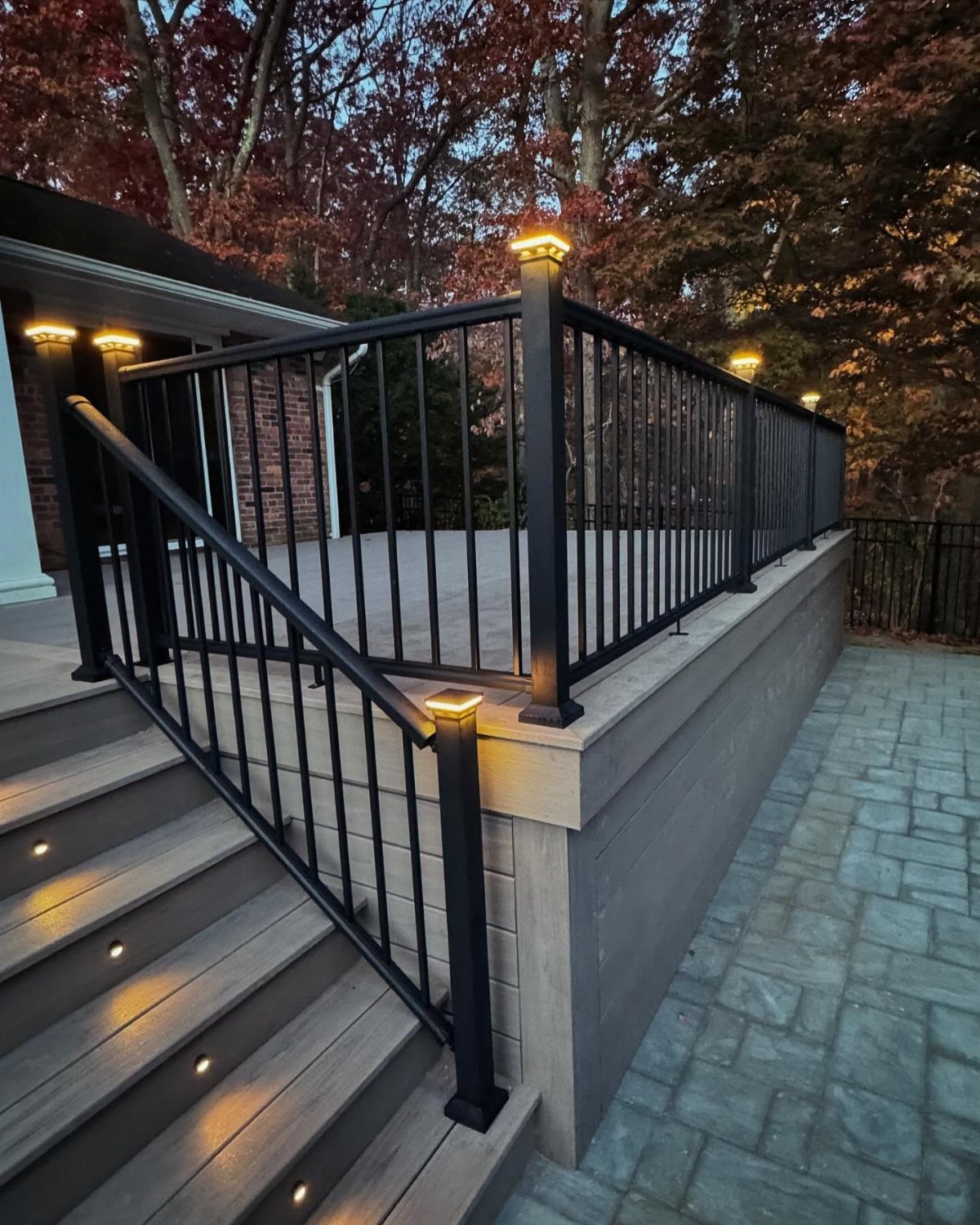 Grey composite deck with black railings and warm recessed lights on stairs and posts.