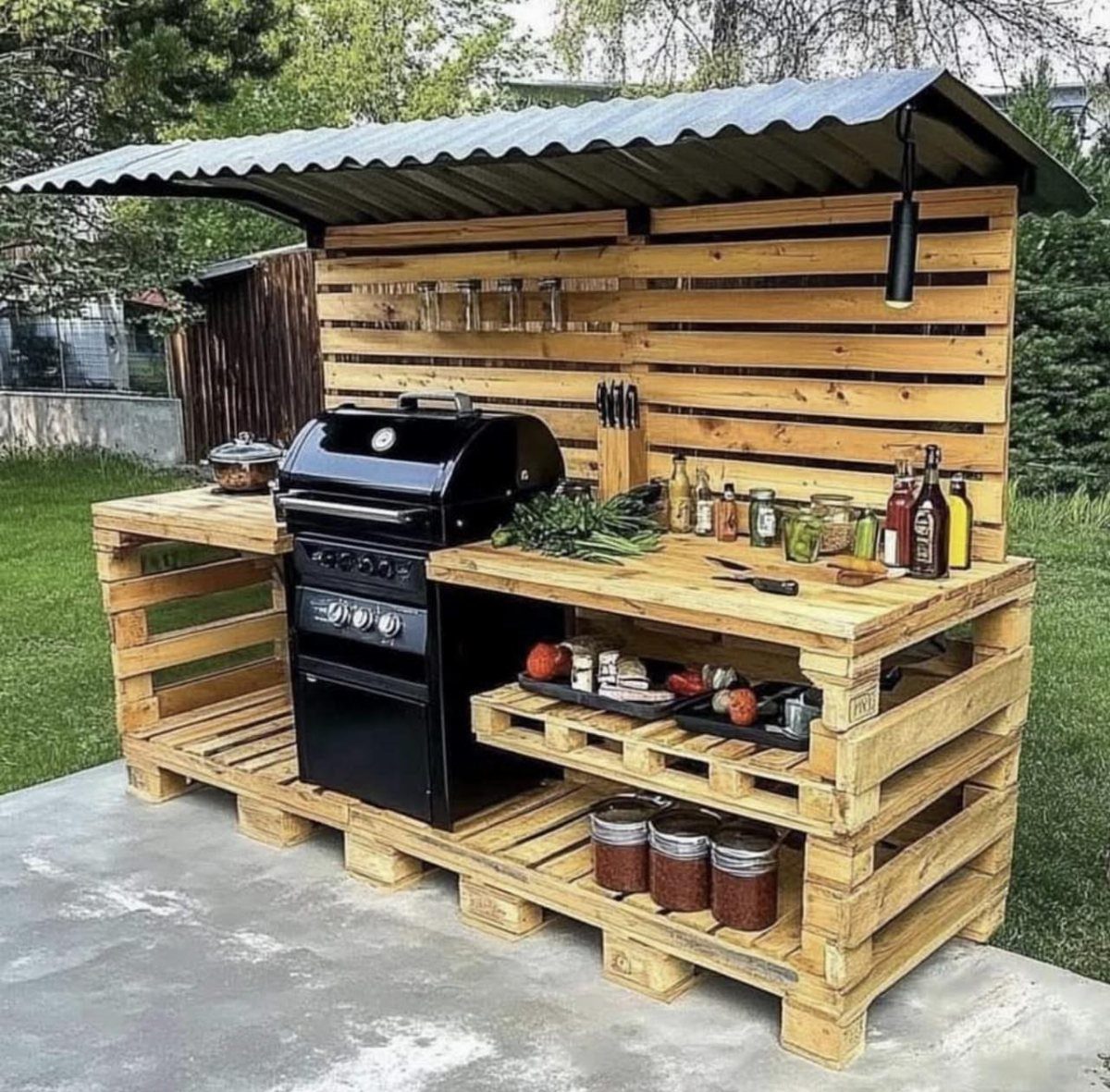 Pallet Grill Station: 7 Outdoor Builds from Cart to Kitchen 6 A pallet wood outdoor kitchen station featuring a black gas grill and various cooking supplies.