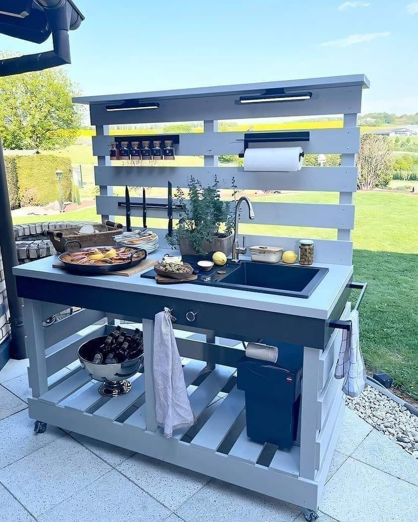 Pallet Grill Station: 7 Outdoor Builds from Cart to Kitchen 5 Grey pallet outdoor kitchen station with a dark countertop, integrated sink, and various cooking accessories.