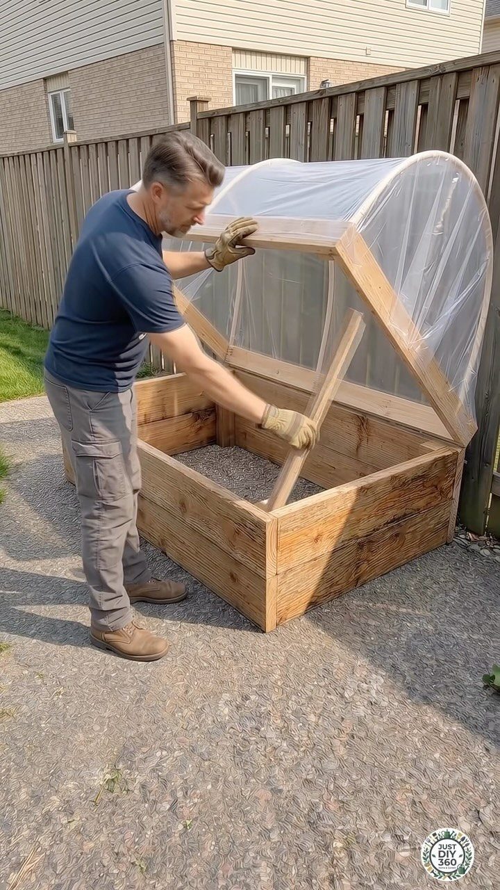A man working on a wooden raised garden bed with a clear plastic cover.