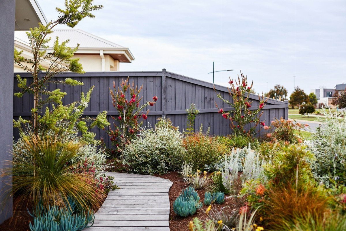 16 Small Home Landscaping Ideas That Fit Any Plot 7 Various shrubs, grasses, and red flowering plants arranged in a small landscaped garden bed.