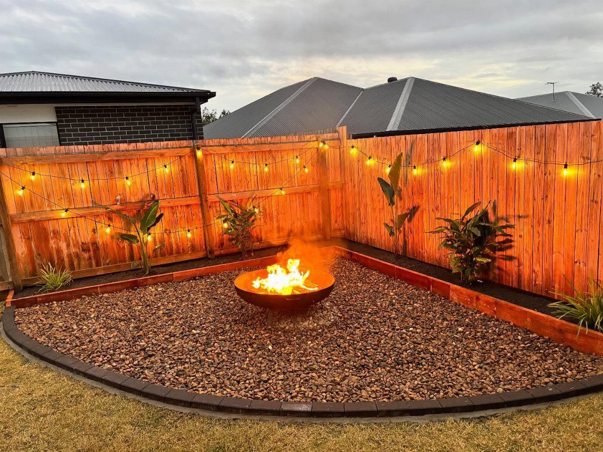 16 Small Home Landscaping Ideas That Fit Any Plot 4 A burning metal fire bowl centered in a gravel courtyard enclosed by a wooden fence.