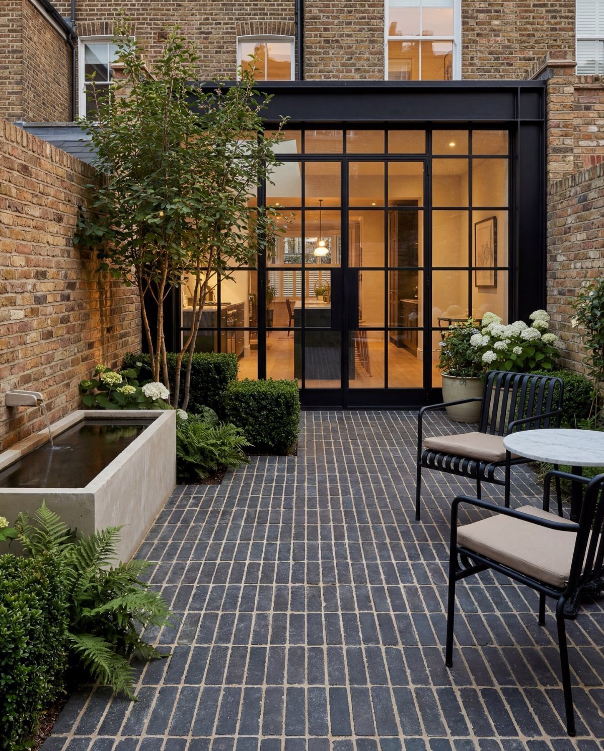 16 Small Home Landscaping Ideas That Fit Any Plot 12 Manicured green shrubs and a small tree planted in a brick courtyard next to a water feature.